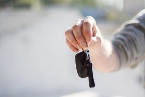 A hand holding a car key and remote fob against a blurred outdoor background