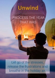 A child holds a glowing sky lantern at dusk with the words Unwind, Process the year that was and holiday text
