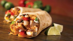 Two fish tacos wrapped in flour tortillas filled with grilled fish peppers and onions served with lime wedges