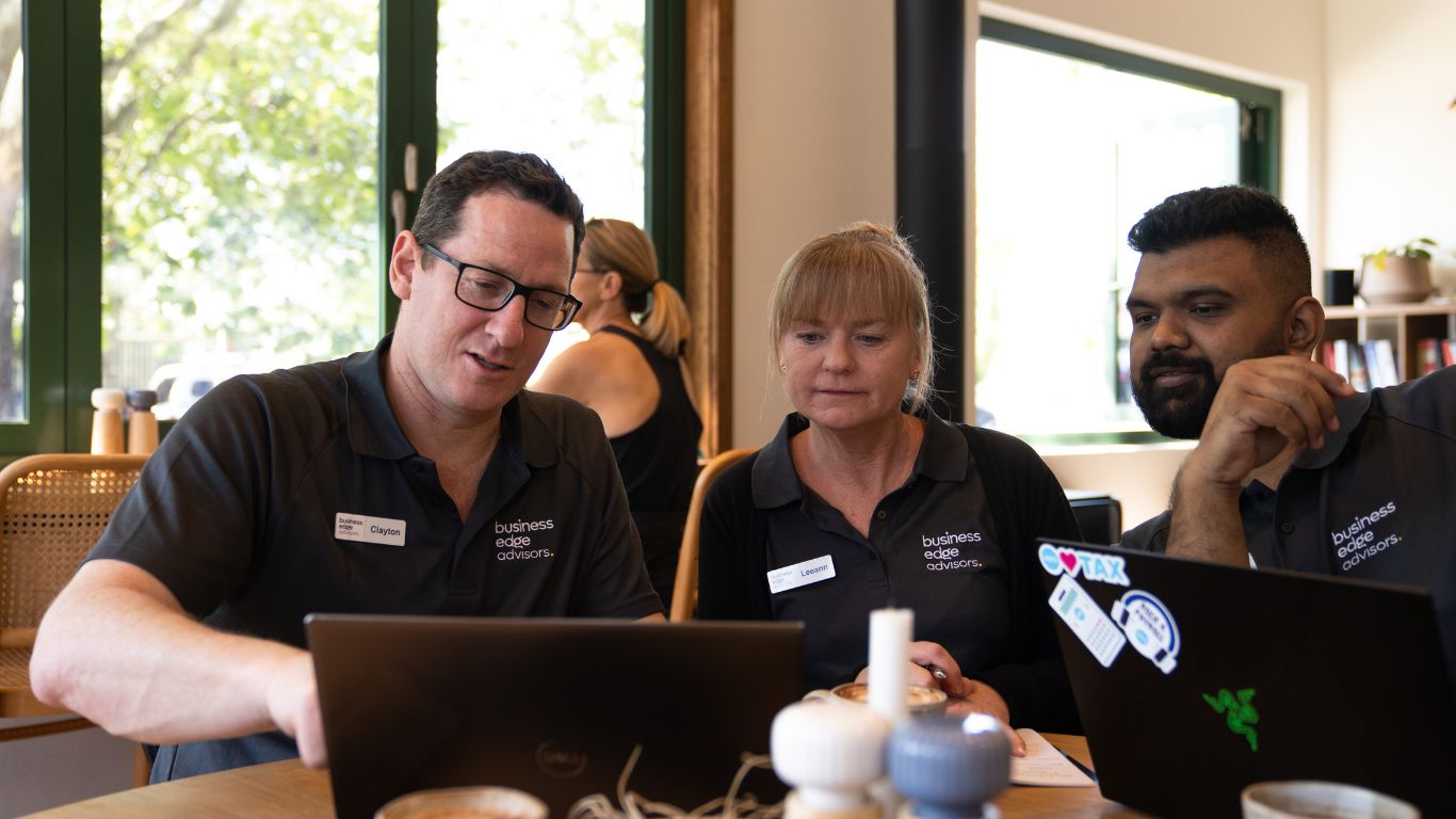Three people in branded shirts work on laptops at a table in a bright cafe setting