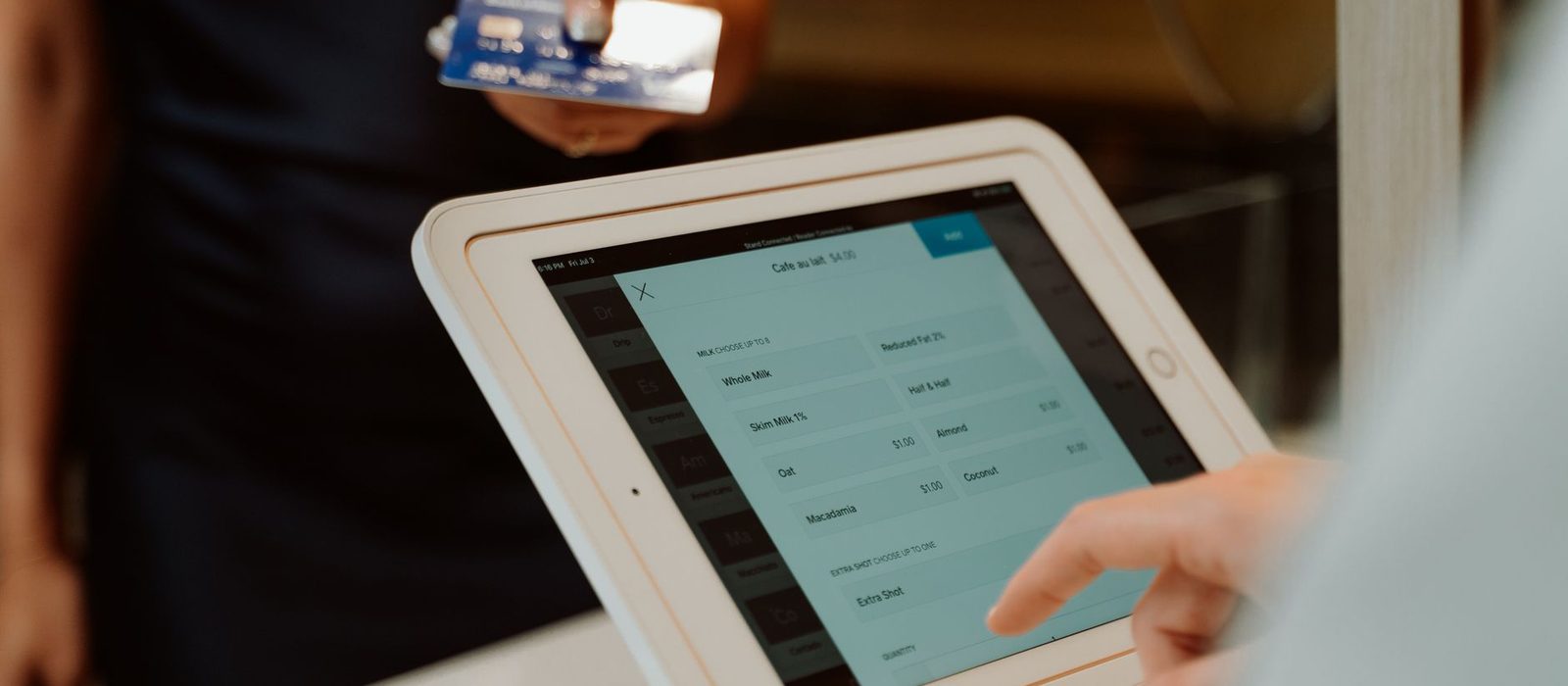 A customer holds out a card to a tablet point of sale screen showing a four dollar coffee order