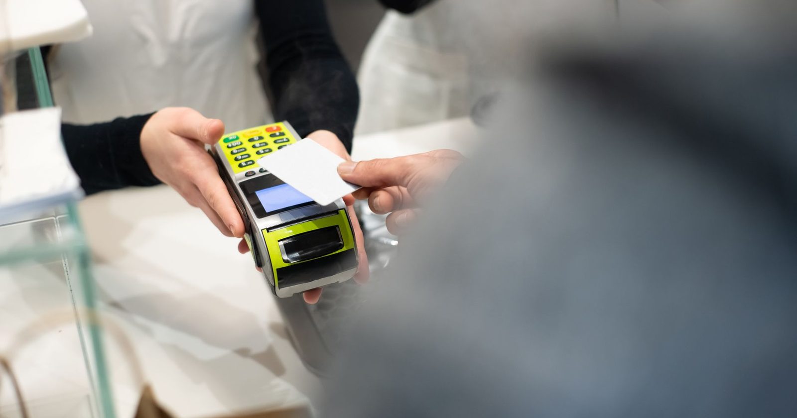 A shop assistant holds a card terminal out across a counter as a customer reaches for it