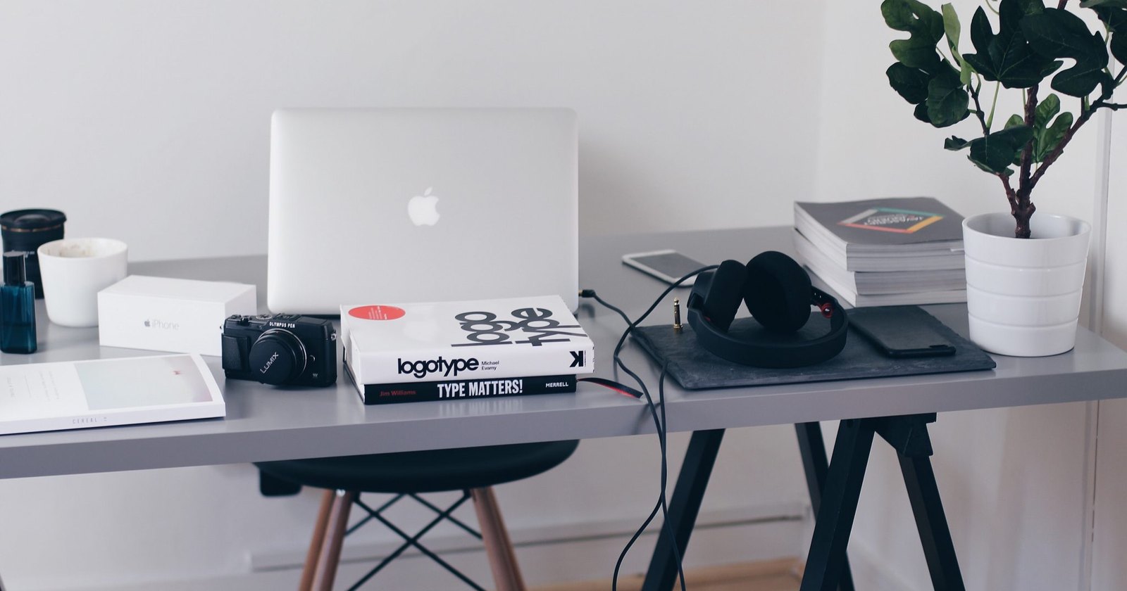 A home office desk with a laptop headphones notebooks and a pot plant