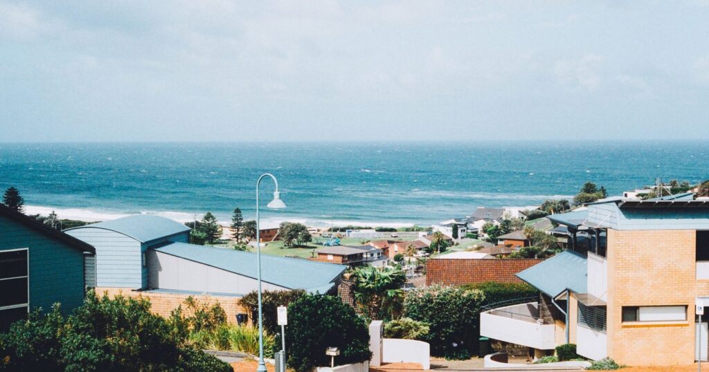Weatherboard and brick holiday houses on a hill above a surf beach, with whitecaps on the sea behind them