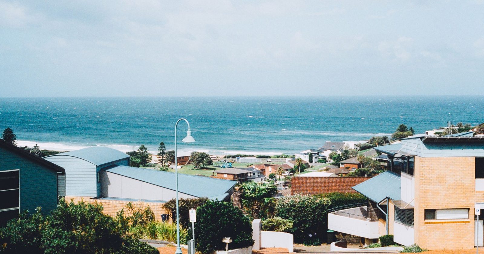 Weatherboard and brick holiday houses on a hill above a surf beach with whitecaps on the sea behind them